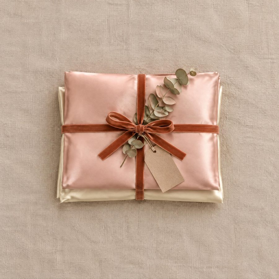 Blush-pink and champagne silk pillowcases folded and tied with a terracotta ribbon and a gift tag